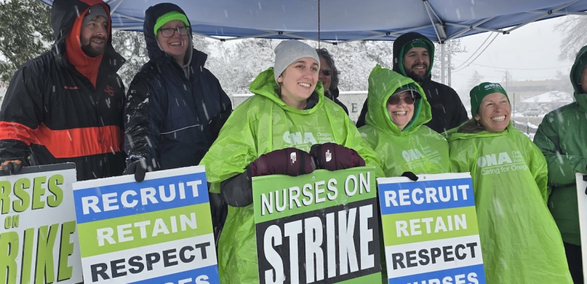 Six smiling people with green and blue strike signs stand under a tent in the snow.