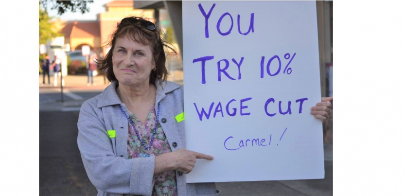 woman outdoors holds sign: "You try 10% wage cut Carmel!"
