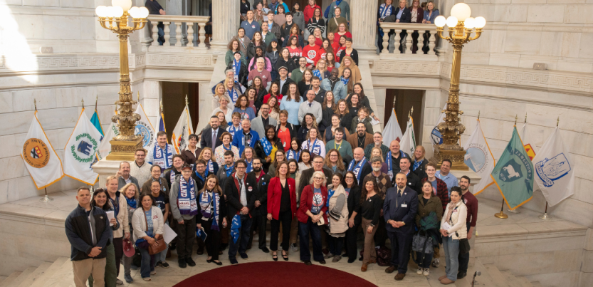 Fifty people pose on the stairs inside the Rhode Island capitol.