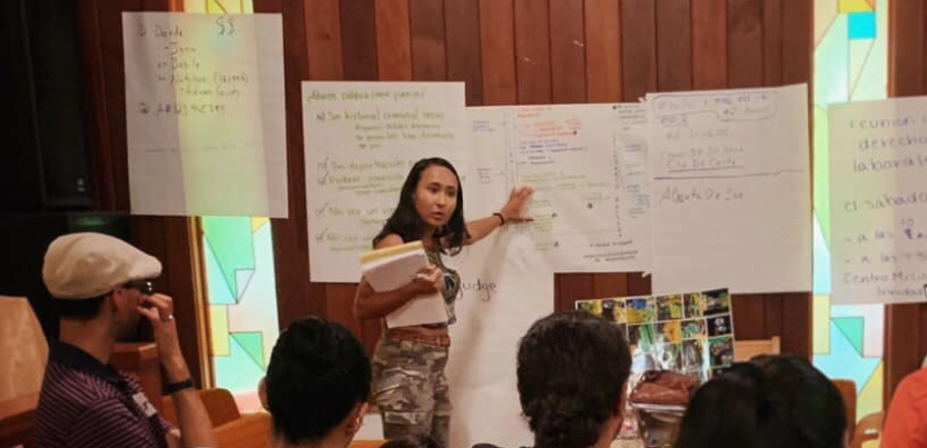 Woman leads organizing meeting from front of room.