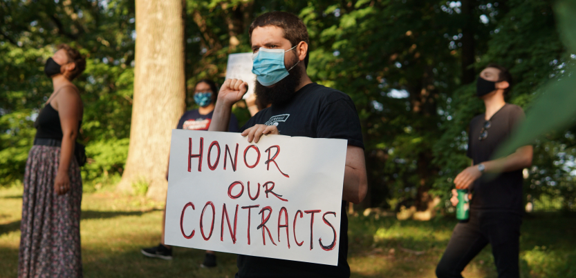Masked person holding sign "Honor Our Contracts" in front of trees, other masked demonstrators