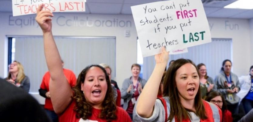 Two teachers holding signs. Tiffany's sign says "You can't put students first if you put teachers last."