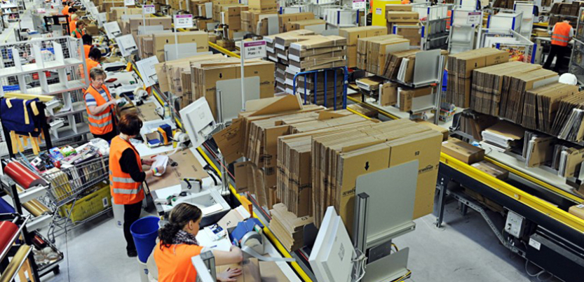 Amazon warehouse with goods on shelves and workers in orange vests working.
