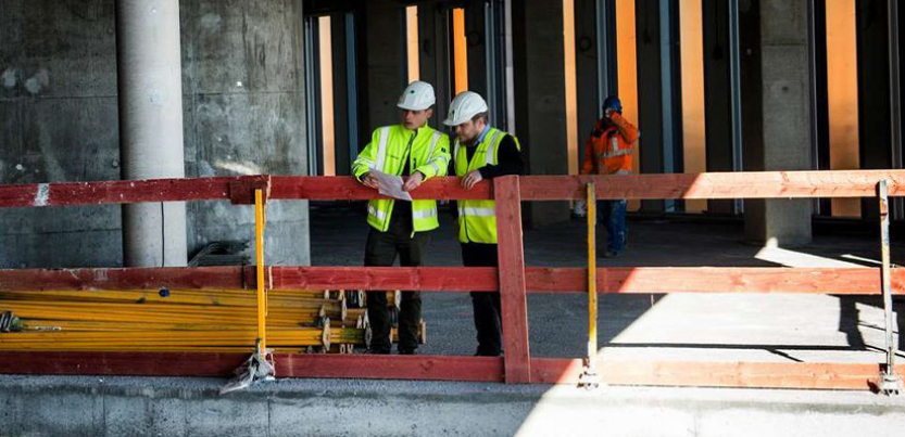Two construction workers looking down in building construction site with wooden scaffolding around them.