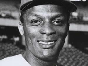 Center fielder Curt Flood smiles in a close-up head shot with stadium seating behind him.