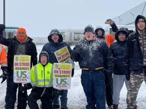 A group of workers stands in the snow and cold outside a US Foods yard in Spokane, Washington holding signs that say Local 705 Teamsters On Strike Against US Foods.