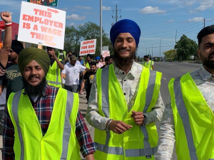 Members of the Naujawan Support Network march holding signs that say "This employer is a wage thief."