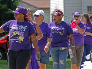 A group of black and white workers wearing purple SEIU T-shirts march.