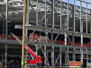 Metal ribs and girders of a factory being constructed are visible, with a red construction crane