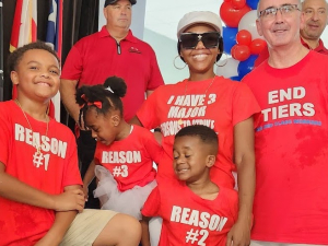 A young Black woman and her three children, all in red shirts, pose with UAW president Shawn Fain, a white man, also in a red shirt.