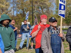 A group of workers looks to the left, with signs saying UAW on strike