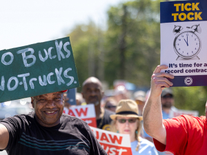 Auto workers with signs saying no bucks, no trucks and Tick Tock Time for a Record Contract march towards the camera