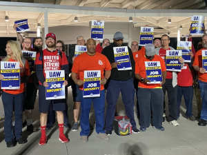 Workers in red shirts stand in a row with UAW signs