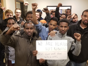 Amazon workers with fists raised gathered around a sign.