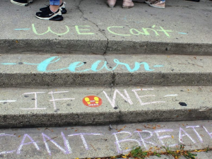 Steps chalked in blue and pink with the words we can't learn if we can't breathe with a few students feet and shoes visible