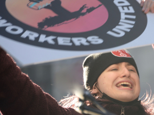 Woman in a warm hat holds Starbucks Workers United sign high with sun behind her