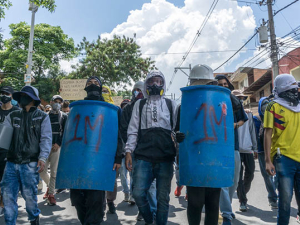 Row of protesters blockading the street in Colombia, two of whom are wielding blue shields of some kind.