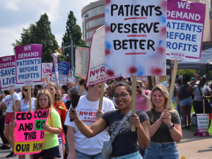 A group of nurses hold picket signs by a street