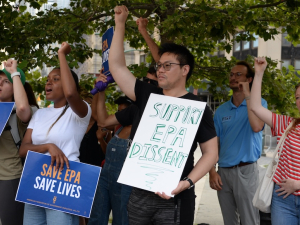 Several people raise their fists, one holds a homemade sign saying “support EPA dissent”