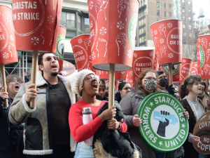 A crowd raise huge red cups that say “Baristas on Strike”