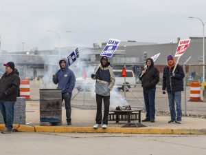 Workers six workers seen from far away hold picket signs by a burn barrel.