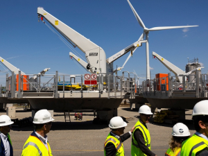 A group of people in hi-viz vests and hardhats walk by huge turbine components
