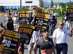 A big group of men marches, carrying black-and-yellow picket signs that say: "Amazon workers on ULP strike, united for $30 an hour and safe jobs" with a Teamsters logo