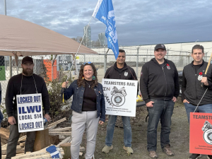 A group of people hold picket signs in front of a canopy.