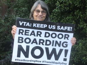 Woman holds sign reading "VTA: Keep Us Safe! Rear Door Boarding Now! #RearBoardingNow #TransitEquityDay"