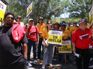 One Black man and several Asian and Latina women hold strike signs in a hotel parking lot.