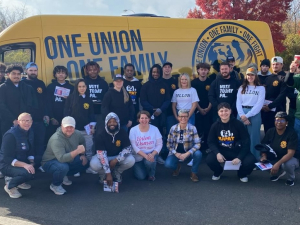 Thirty people pose with a yellow van behind them that says One Union, One Family