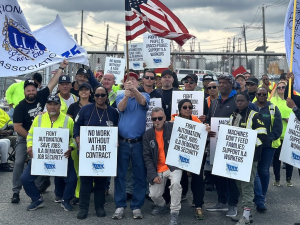 Thirty workers with ILA flags line up for the camera, smiling and waving signs