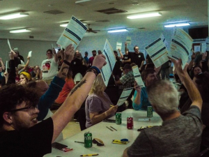 60 people at tables hold papers high in the air