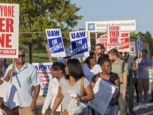 Group of UAW strkers picketing with signs against tiered wages.