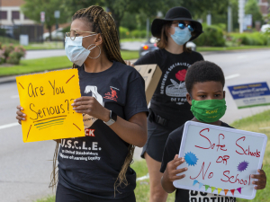 A woman holds a sign that says "Are you serious?", while her son holds a sign reading "Safe schools or no school."