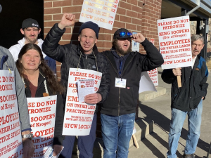 Eight workers hold white and orange strike signs--some have fists in the air and are smiling