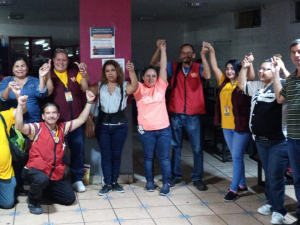 Mexican workers with La Liga gathered indoors in a line with their hands linked and raised in the air