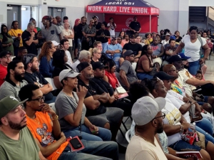 Photo shows a packed hall of autoworkers sitting on folding chairs with standees in the back. 