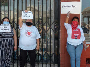 Three women hold signs saying "Food Not Rent" and "Cancel Rent" in English and Spanish.