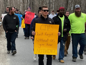 A group of 60, mostly men, a mix of races, marches toward the camera with signs that say “We are One” and “Cives don’t forget without us you have nothing”