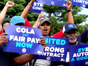 An excited group of six, mostly African American, hold up fists and blue UAW contract campaign signs.