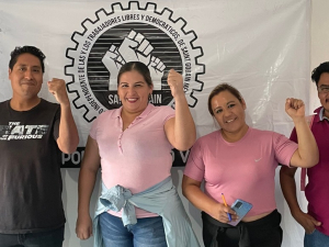 Four members of the bargaining committee at Saint Gobain pose in front of their union's banner.