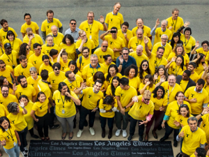 L.A. Times employees gather as NewsGuild members wearing bright yellow shirts around a plaque that says LA Times.