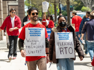 Workers in red shirts march outside the Washington Post's office, carrying signs with slogans including "Flexible RTO" (which stands for return to office) and Washington Post Tech Guild Unite!
