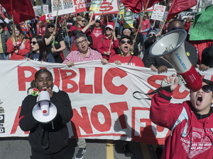 Oakland teachers marching down the street en masse with two bullhorns and a sign.