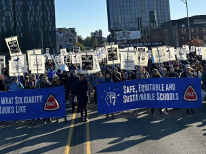 A large crowd in blue marches with banners. One says, “Safe, equitable and sustainable schools” and many carry “ready to strike” signs.