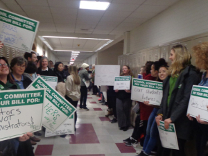 Brookline paraeducators with signs lining hallway of school.