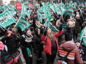 People cheer in a massive packed outdoor crowd with light green flags that say “We are of one voice” in French