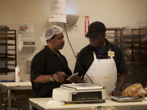 Two bakery workers talk in a kitchen.