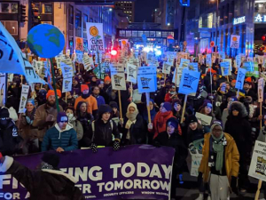 Crowd of climate strikers at night with signs and flags and a banner in downtown Minneapolis.